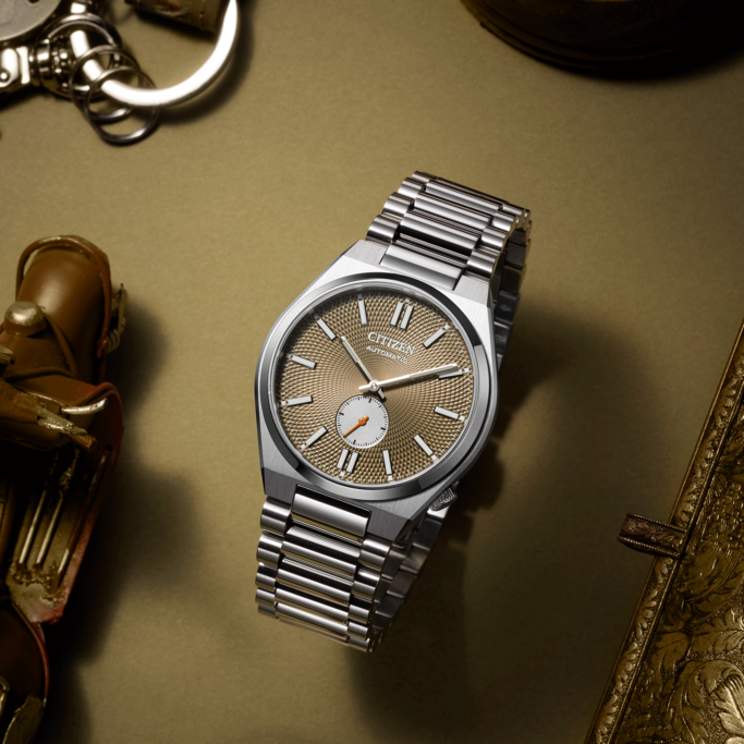 Citizen watch with a silver strap on a golden surface with accessories.