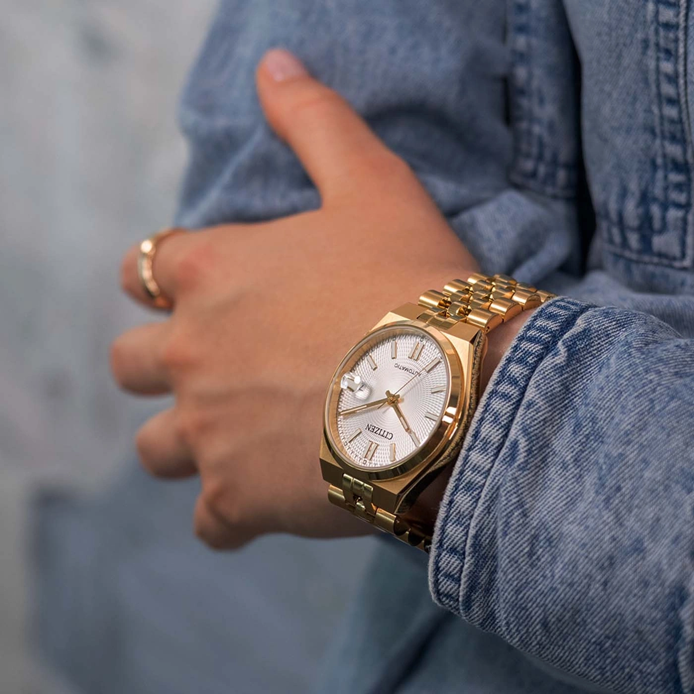 Gold Citizen watch on a wrist in a denim jacket.