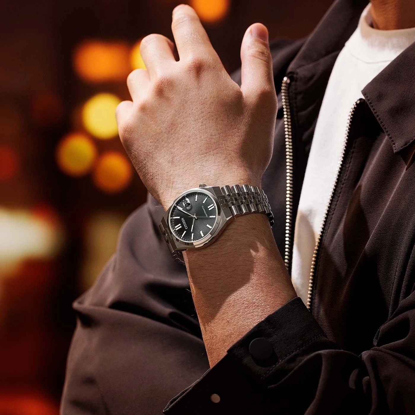 Man wearing a silver watch with a black face and a brown jacket.