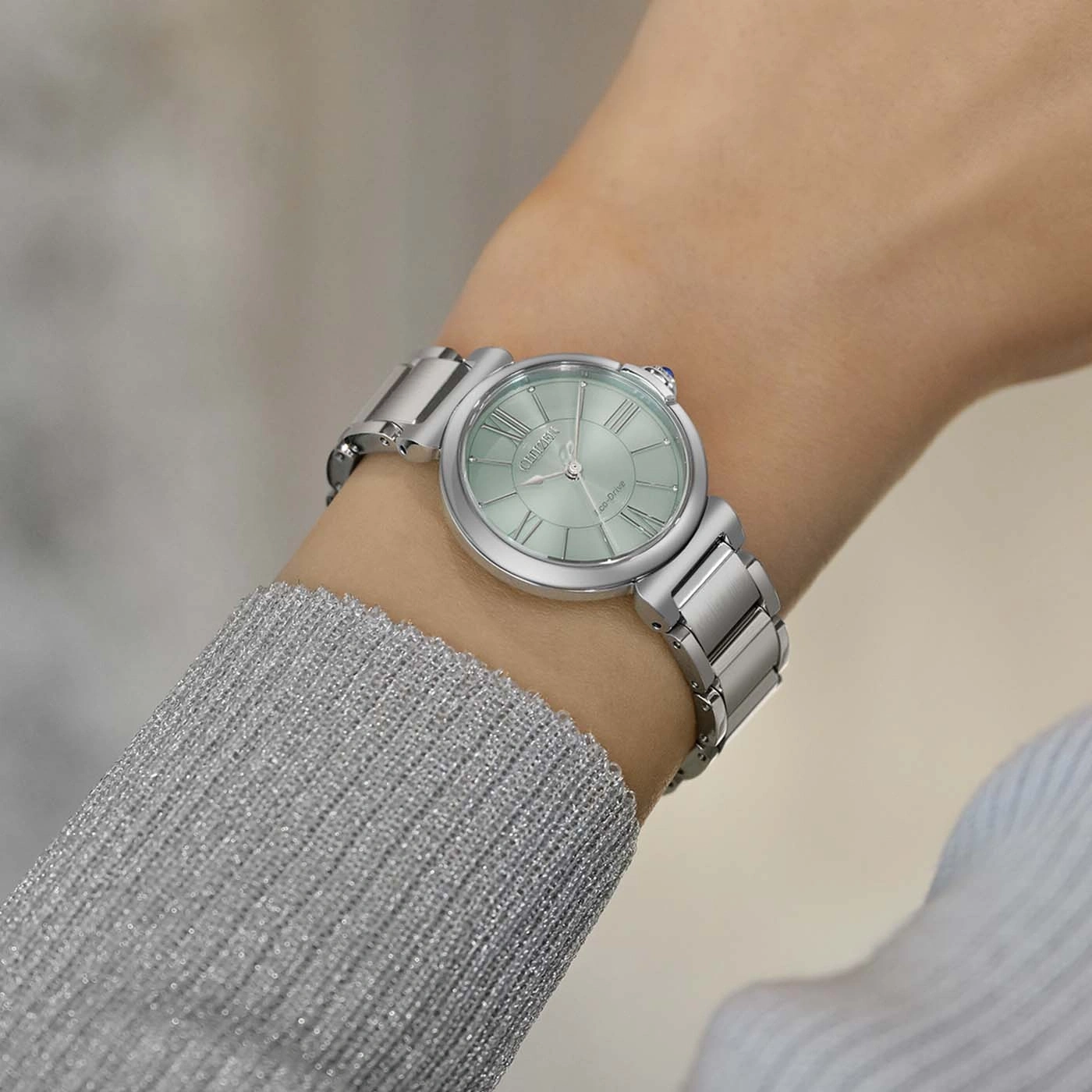 A woman's wrist wearing a silver watch with a light green face.