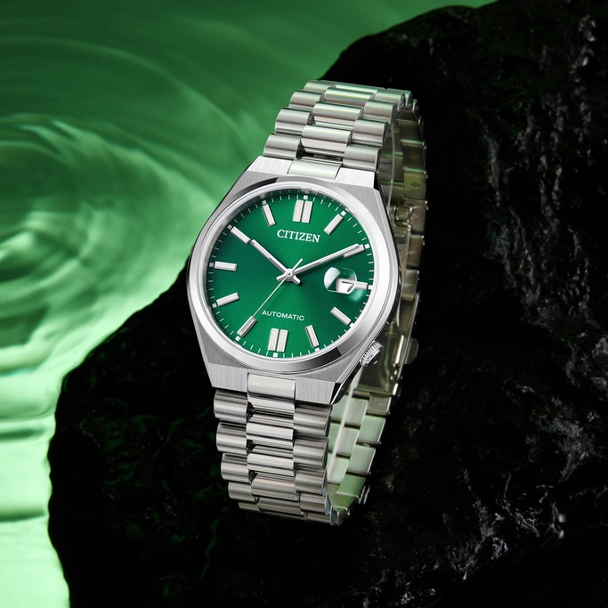 Citizen watch with green face and silver strap on a dark surface.