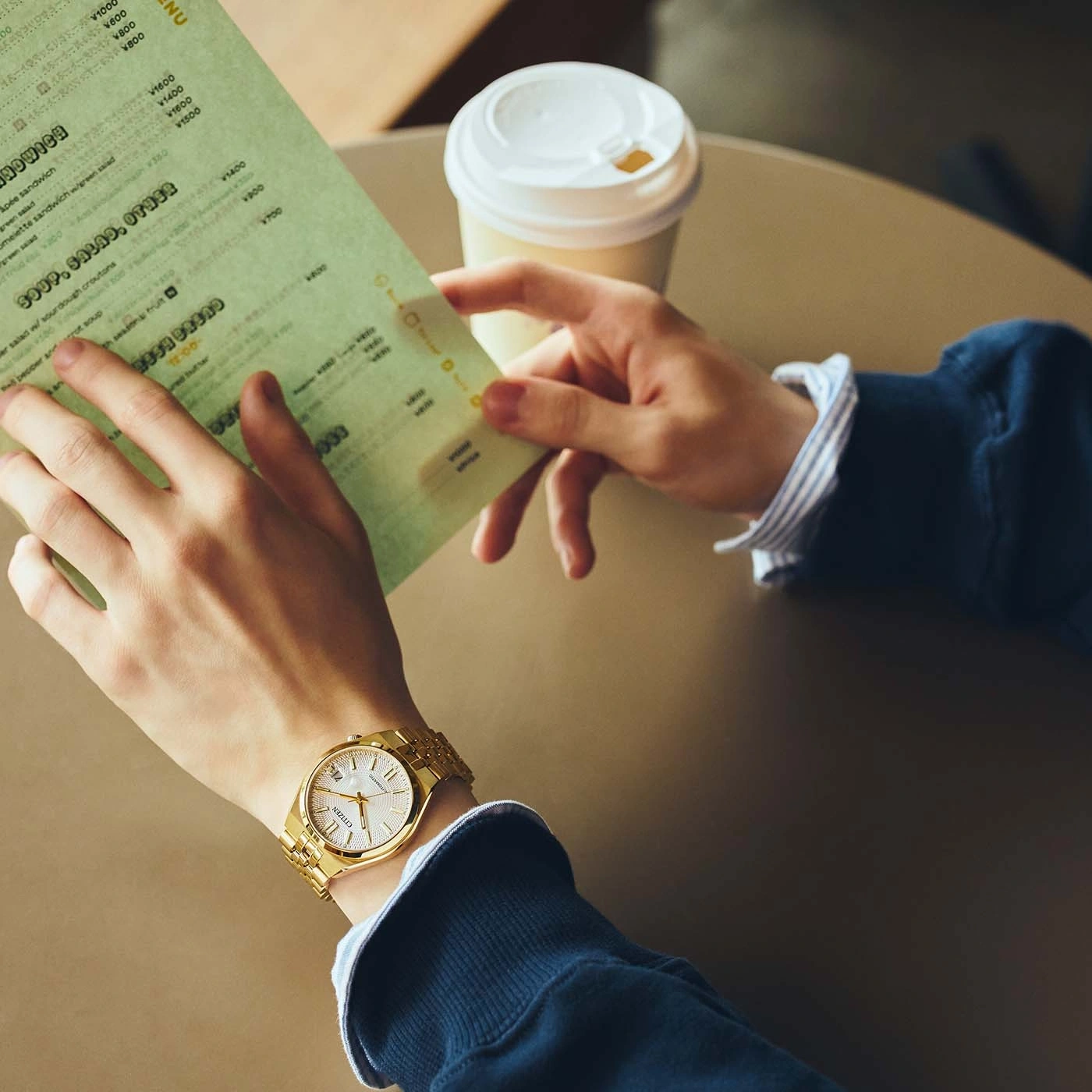 A person is looking at a menu and holding a coffee cup.
