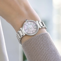 A woman's wrist wearing a silver watch with a mother-of-pearl dial.