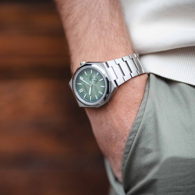 A person wearing a Citizen watch with a green dial and silver bracelet.