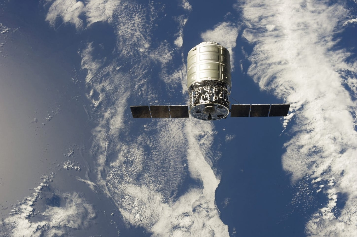 Spacecraft in orbit above Earth with solar panels and clouds in the background.