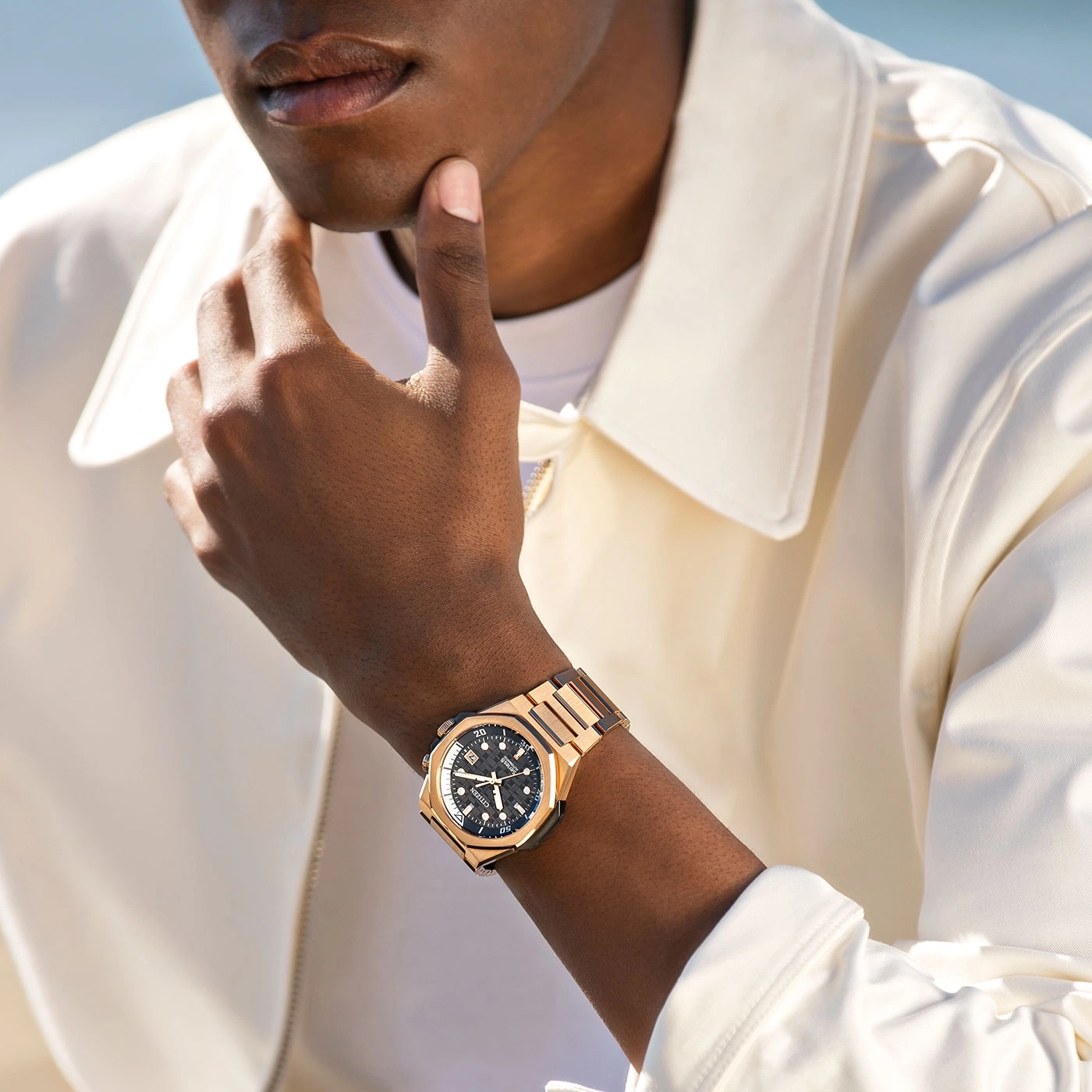 Man wearing a gold watch, posing with his hand on his chin, looking stylish.