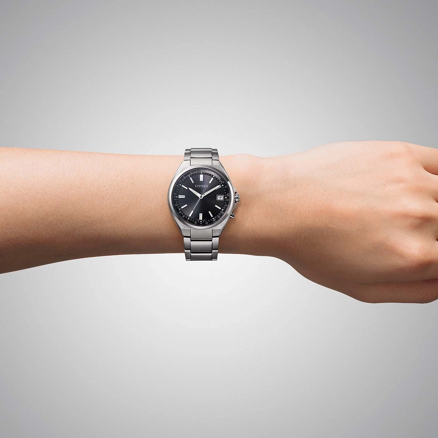 A man's wrist wearing a Citizen watch on a grey background.