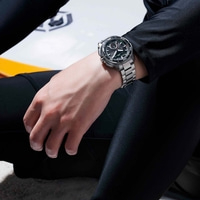 Man wearing a black wetsuit and a watch sitting on a surfboard.