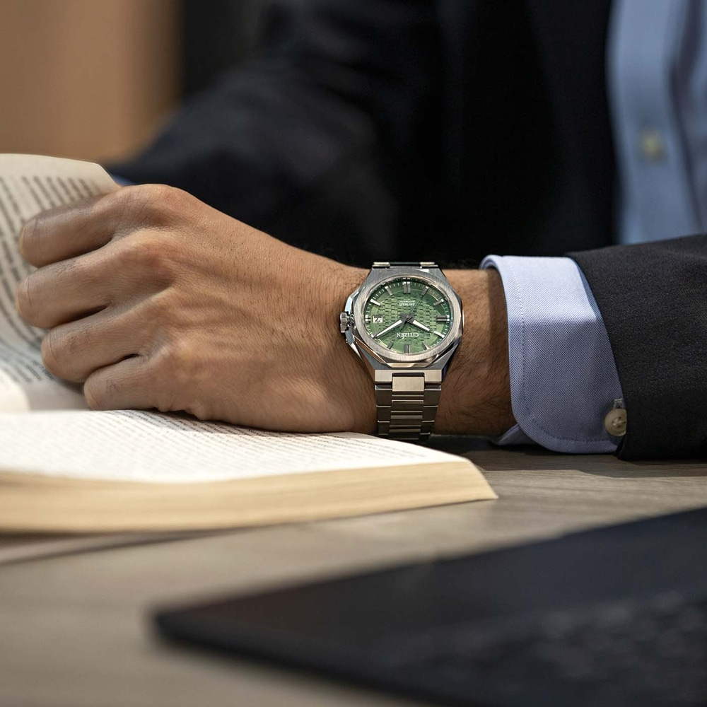 A man in a suit reads a book, wearing a green Citizen watch.
