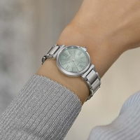 A woman's wrist wearing a silver watch with a light green face.