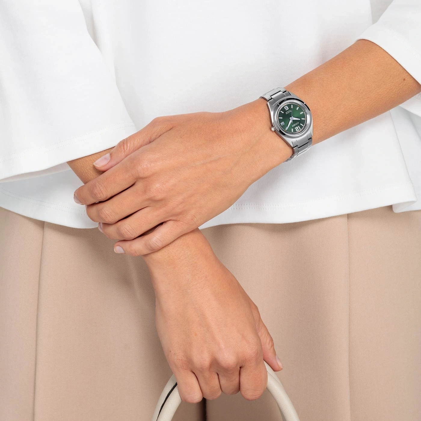 Woman wearing a watch, holding a bag, wearing white shirt and beige pants.