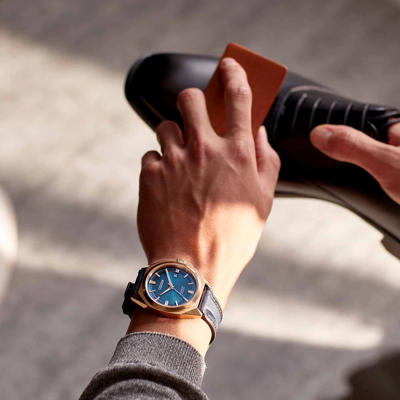 Man polishing a black shoe, wearing a gold watch with a blue face.