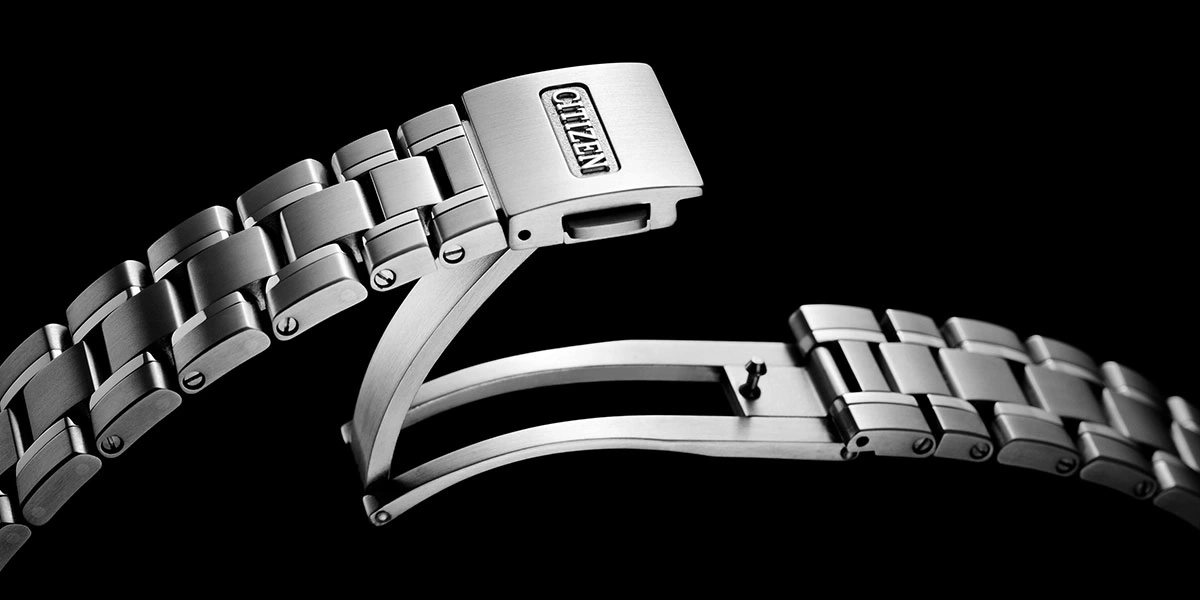 Close-up of a Citizen watch bracelet clasp, stainless steel, black background.