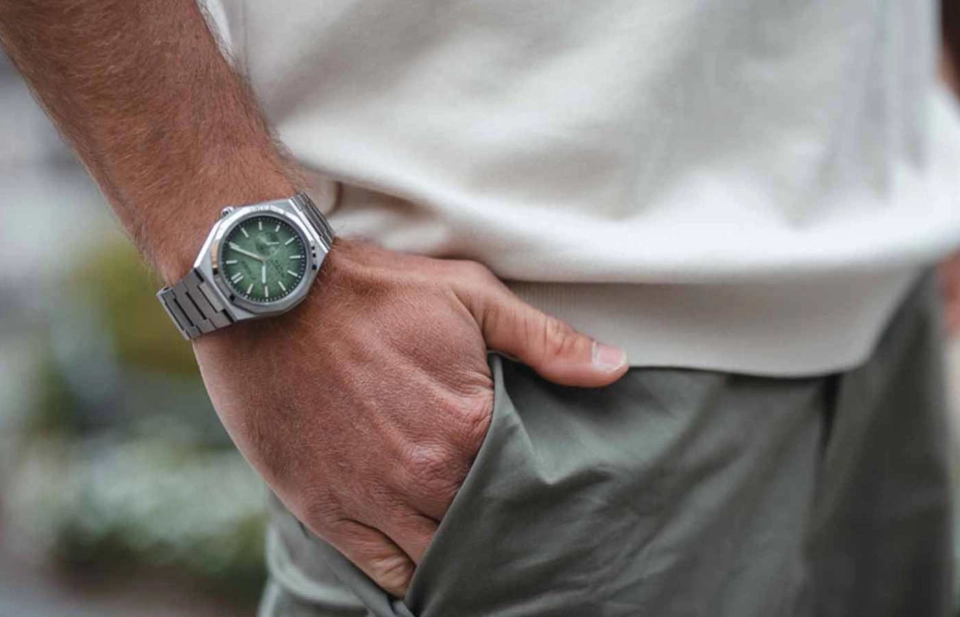Man wearing a watch with a green face, hand in pocket, casual style.