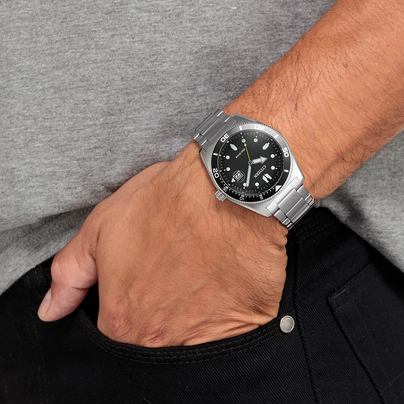 Man wearing a Citizen watch, hand in pocket, black jeans, grey shirt.
