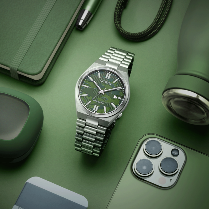 Green watch, phone, notebook, pen, and water bottle on green background.