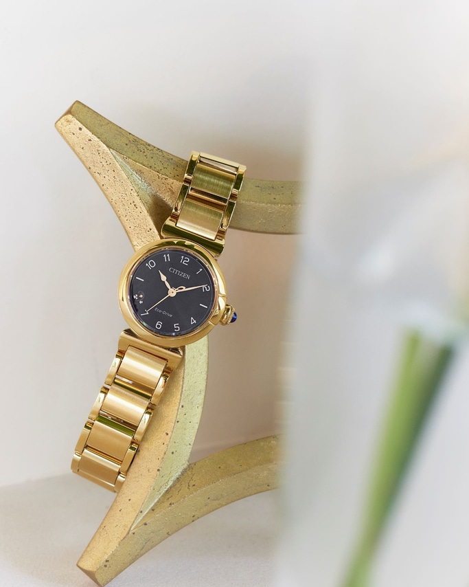 Gold Citizen watch on a gold stand with a black face and gold band.