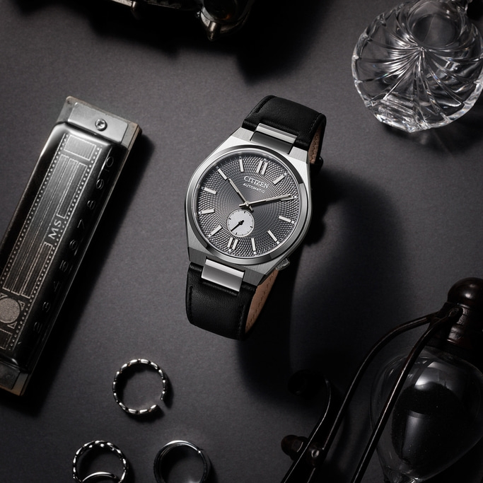 Citizen watch with black leather strap and accessories on a dark surface.