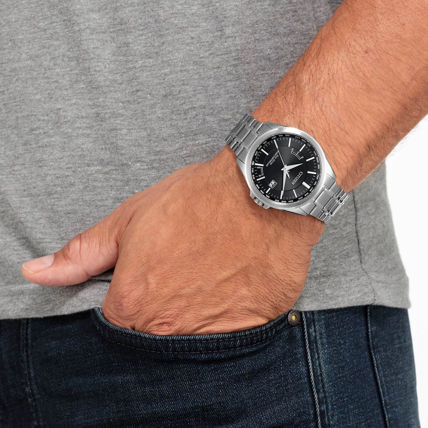 Man wearing a Citizen watch, hand in pocket, gray shirt, blue jeans.