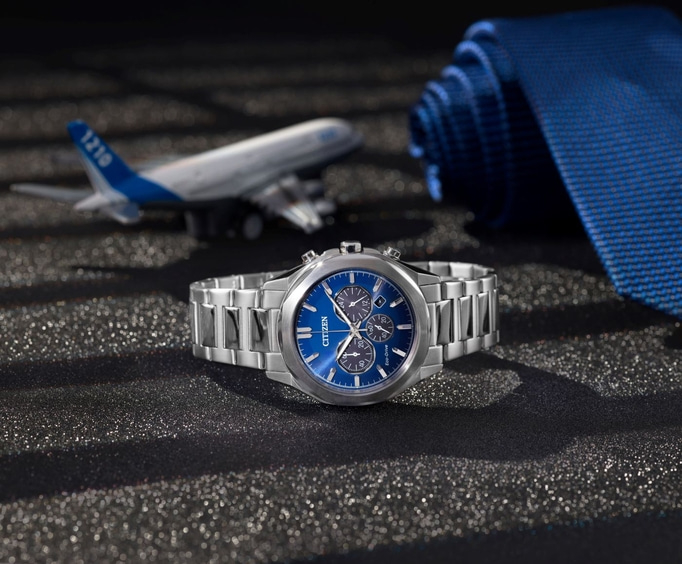 Citizen watch with blue face, airplane, and blue tie on a black surface.