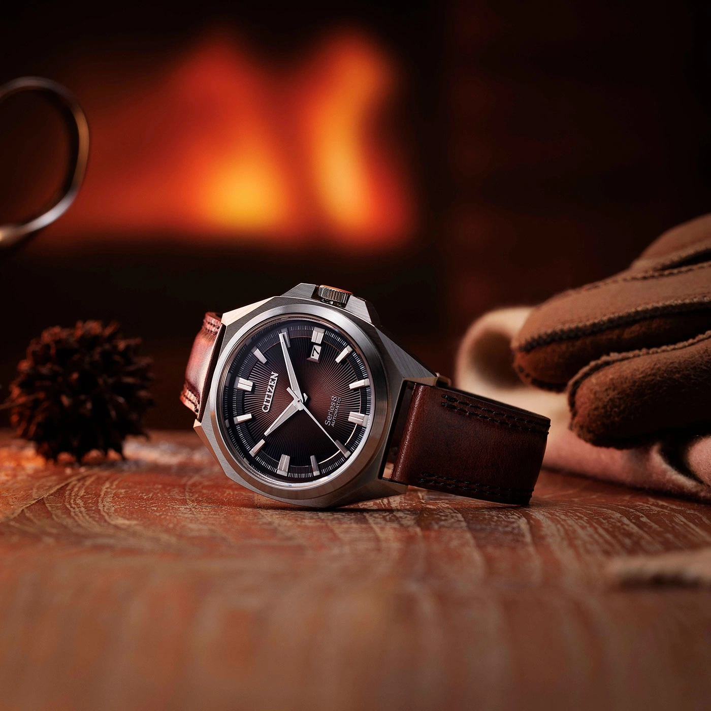 Citizen watch on wooden surface with gloves and a blurred background of a fireplace.