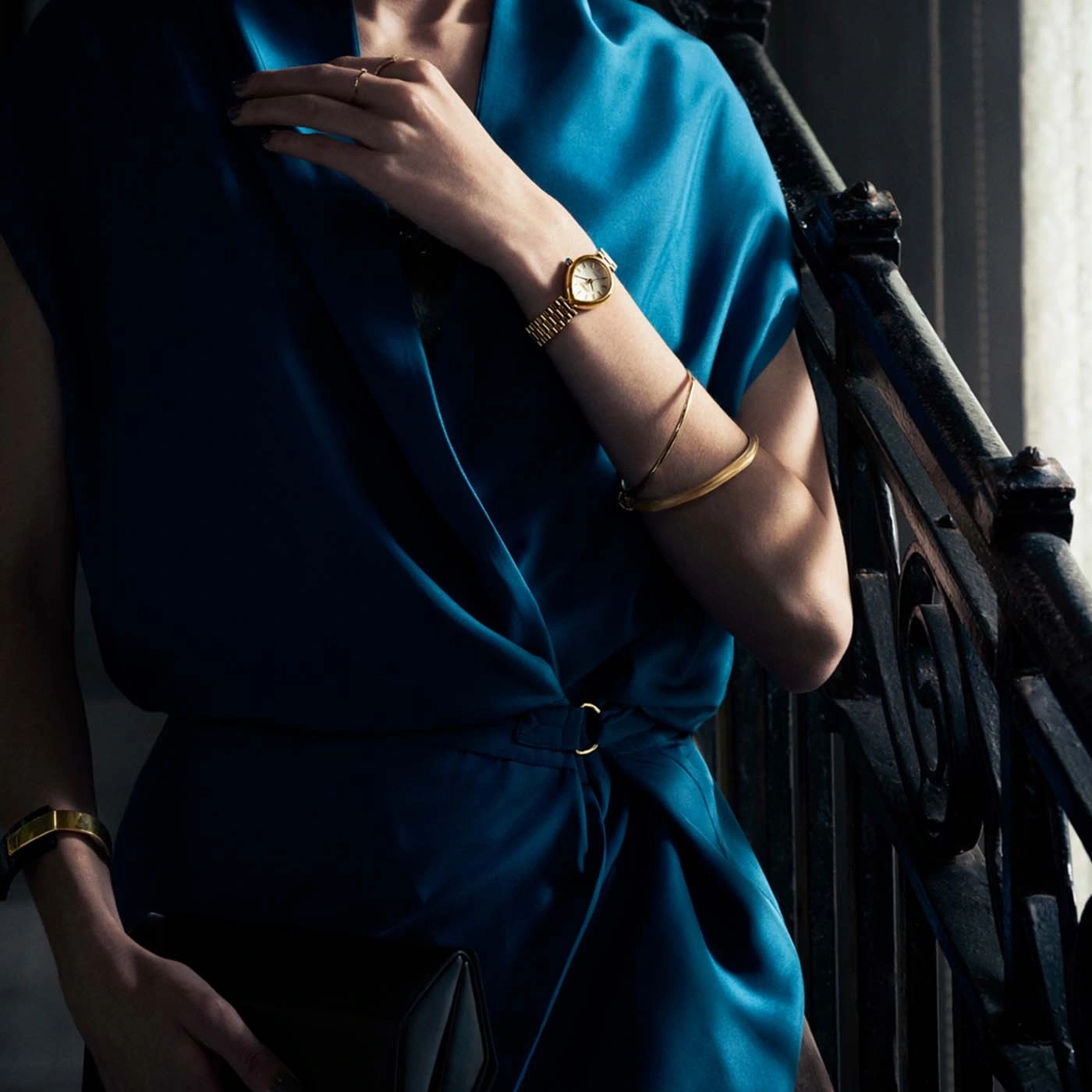 Woman in blue dress with gold jewelry and clutch.