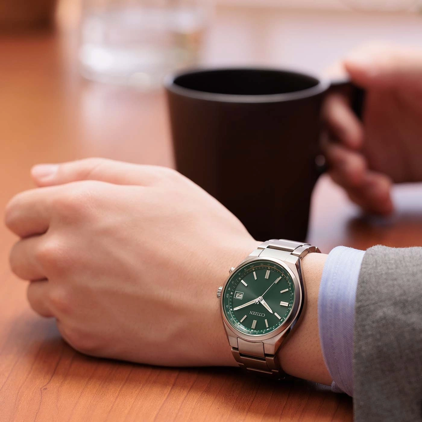 A person wearing a green-faced watch and holding a coffee mug.