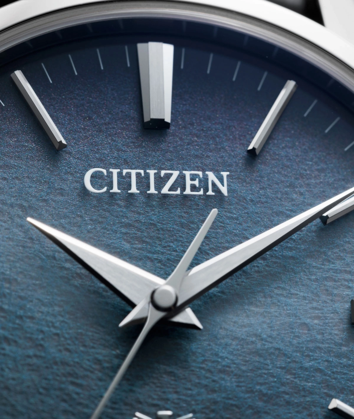 Close-up of a Citizen watch face with silver hands and markers on a blue textured dial.