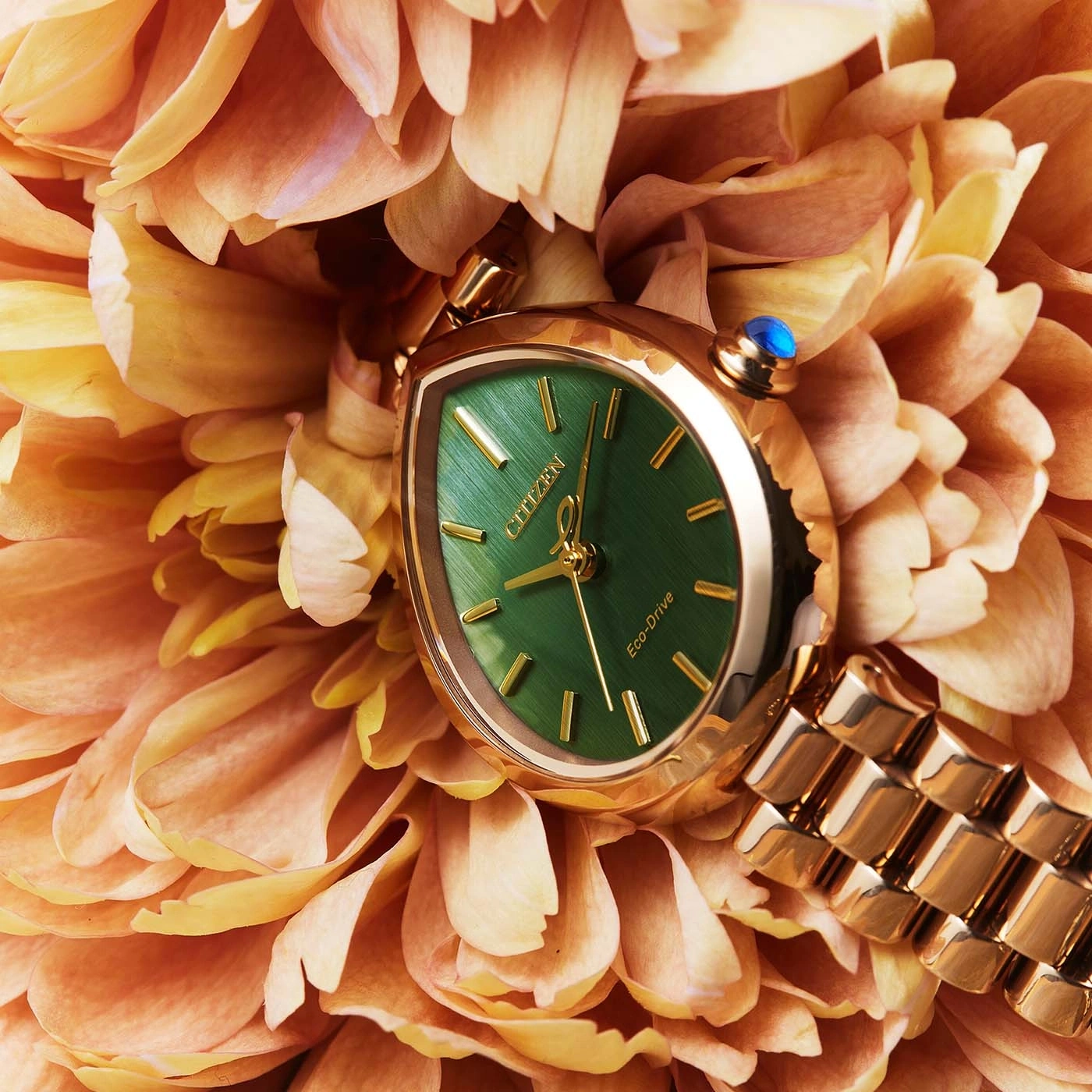A gold watch with a green face rests on orange flower petals.