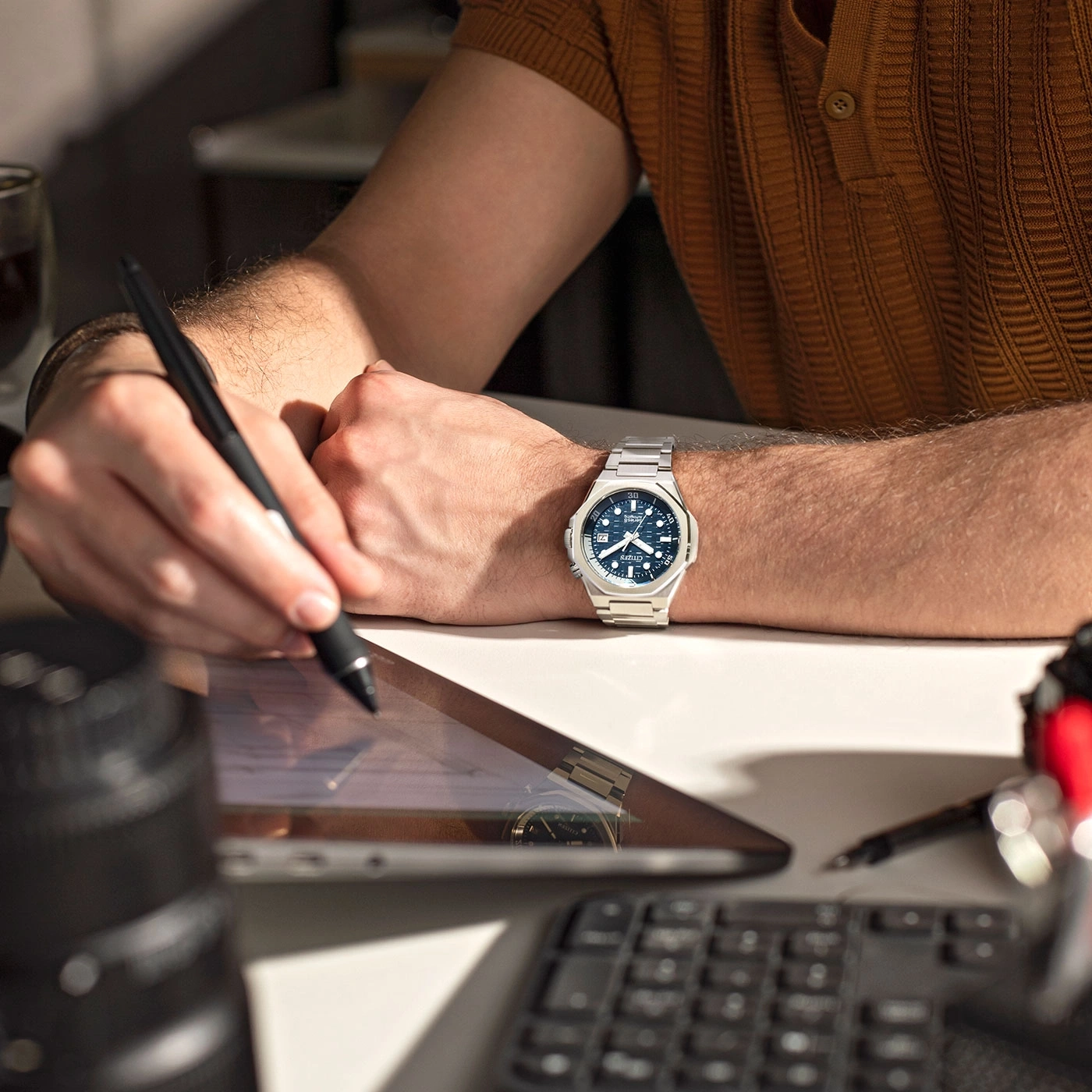 Man working on a tablet with a watch on his wrist and a pen.