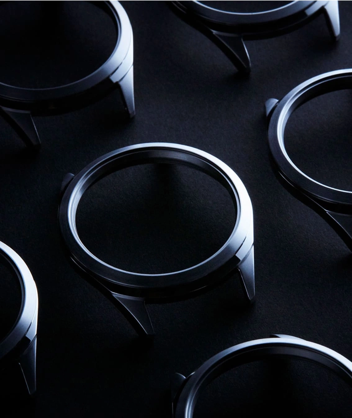 Watch cases arranged on a dark surface, metallic and shiny.