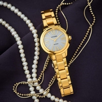 Gold watch with pearl necklace on dark fabric