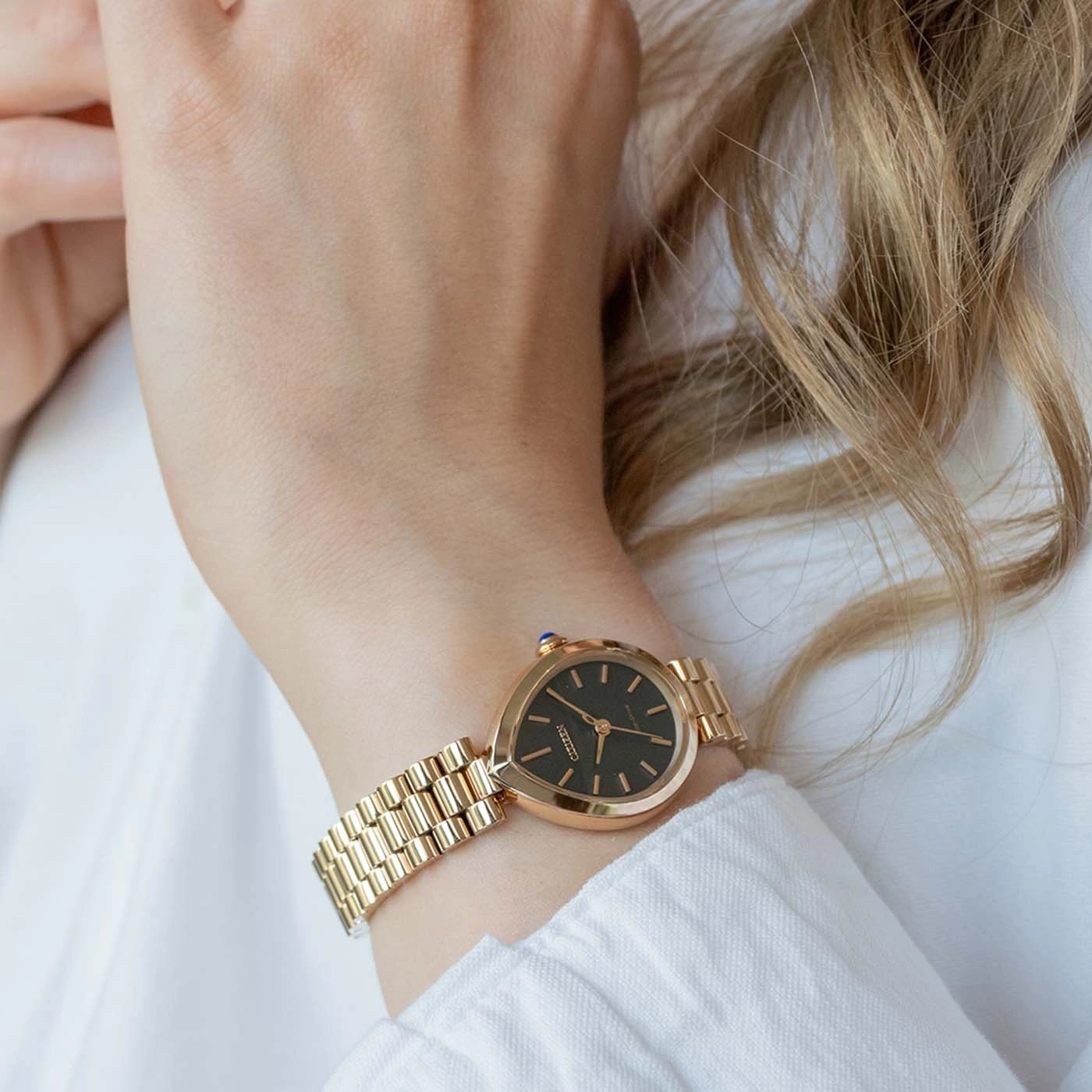 Gold watch on a woman's wrist against a white shirt.