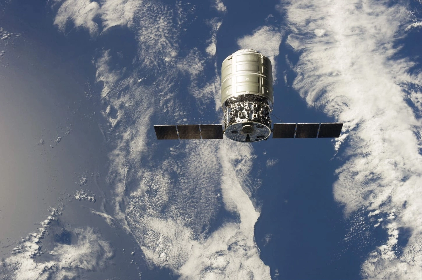 Spacecraft in orbit above Earth with solar panels and clouds in the background.
