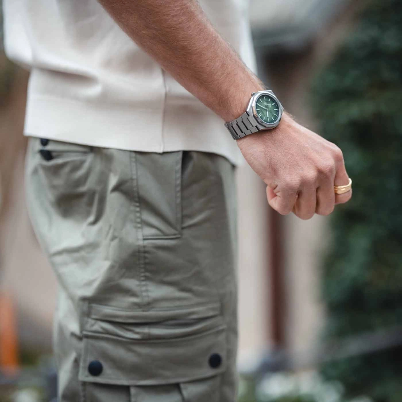 Man wearing a watch and a ring, with green watch face and khaki pants.