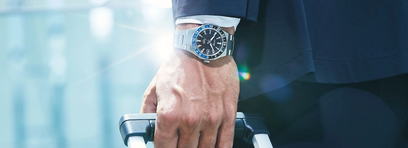 Man wearing a watch, holding a suitcase, traveling in style, business trip.