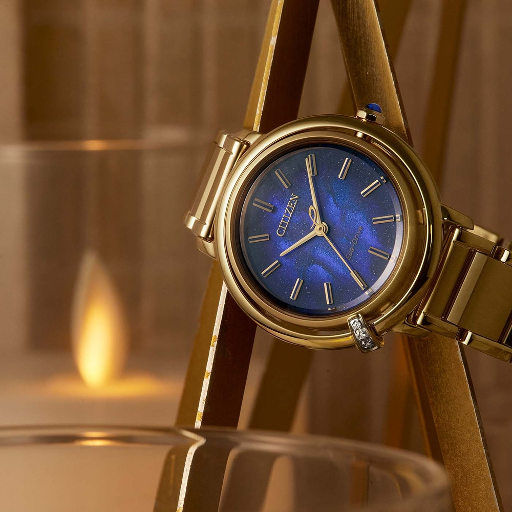 Gold Citizen watch with a blue face, elegant and stylish, with a candle in the background.