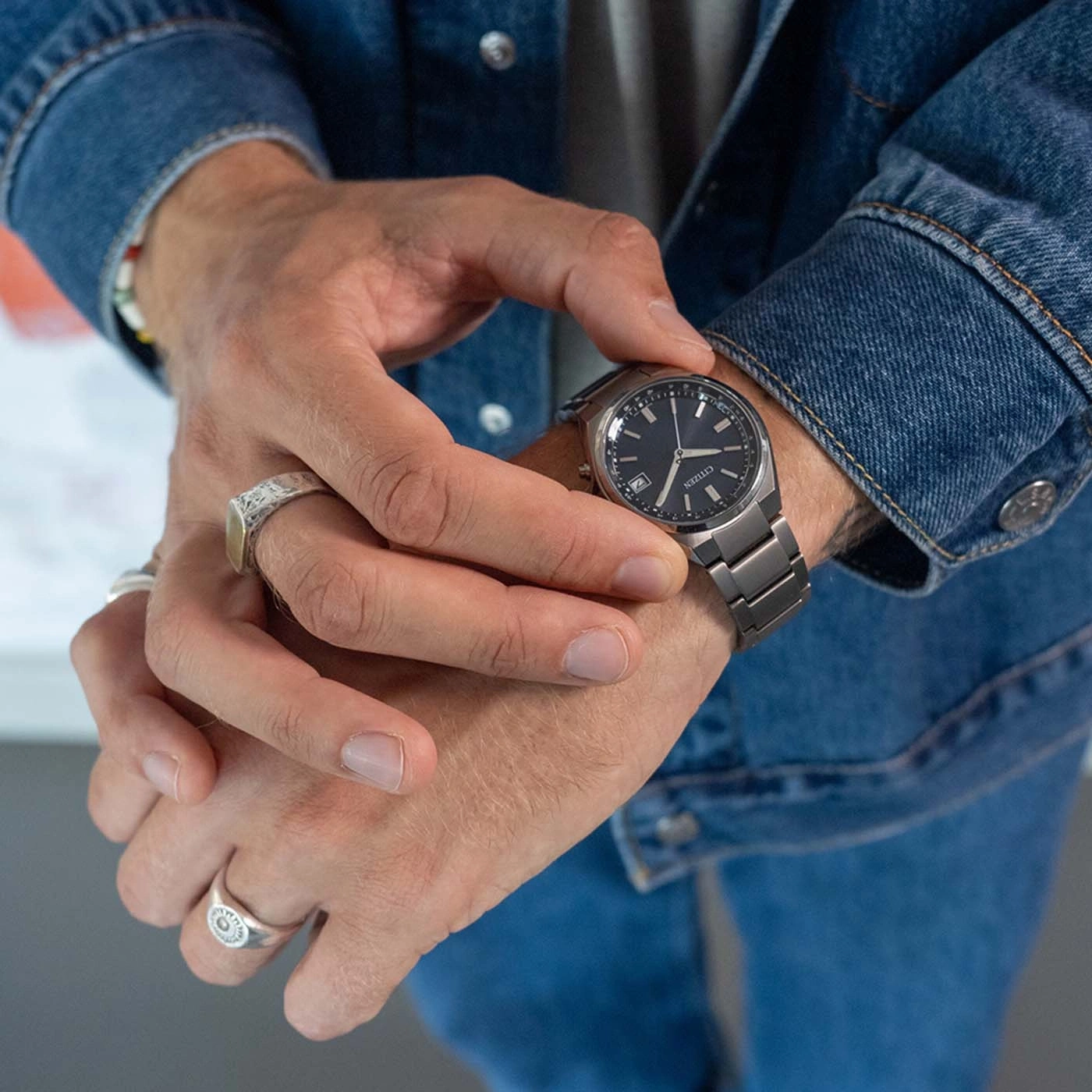Man checking his watch while wearing a denim jacket and rings.