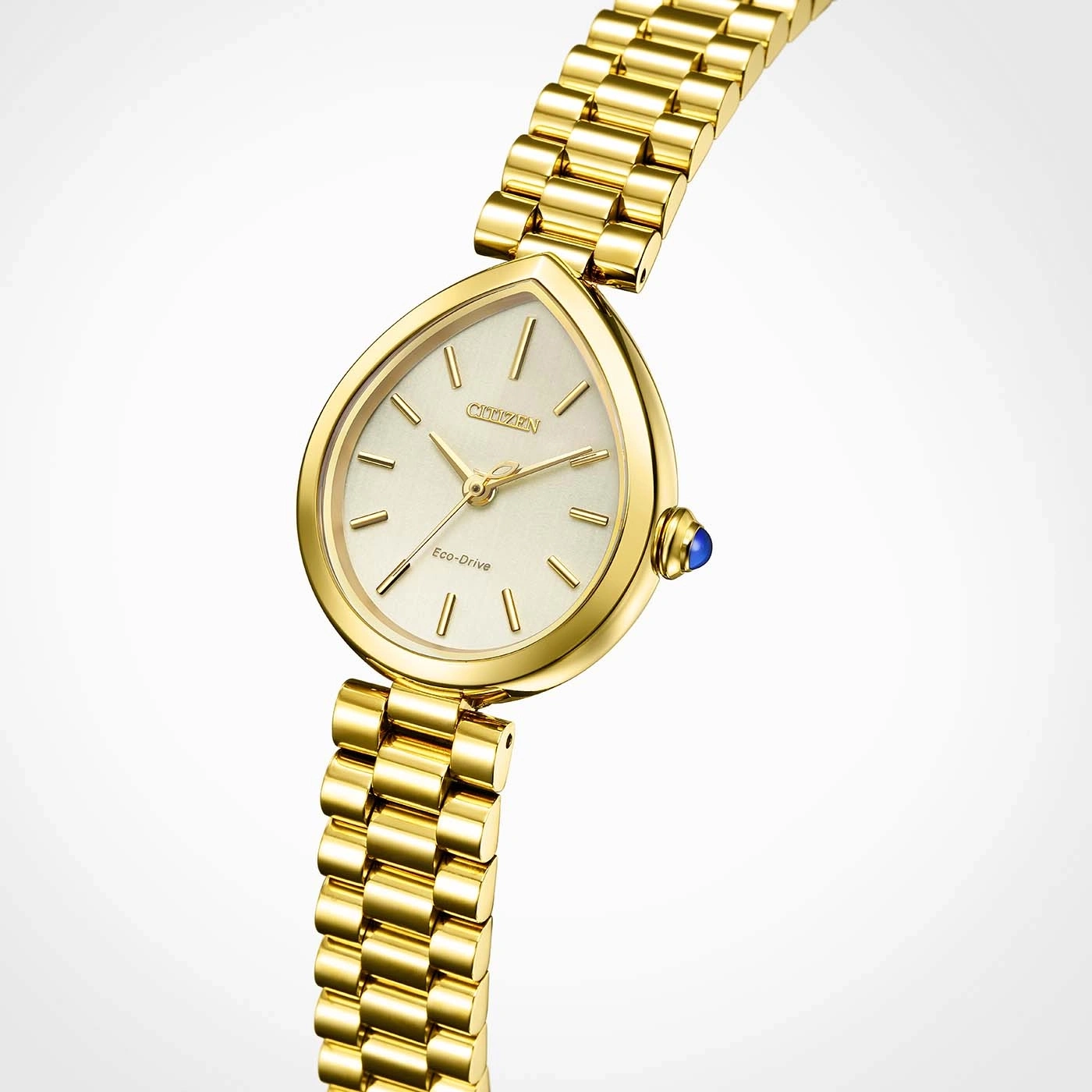 A close-up studio shot of a gold Citizen Eco-Drive watch with a teardrop-shaped face and a blue gemstone on the crown.
