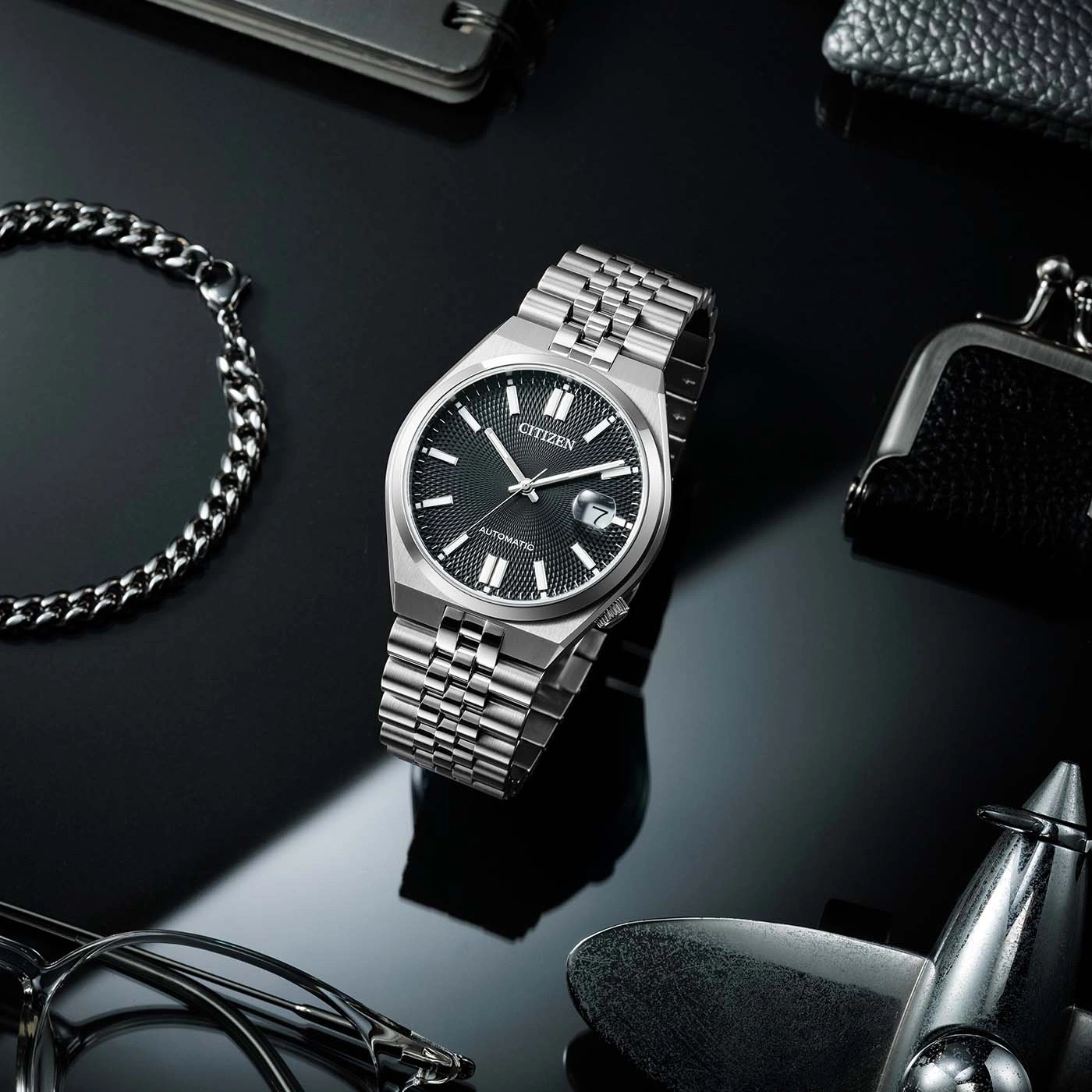 Citizen watch on a reflective surface with accessories, black background.
