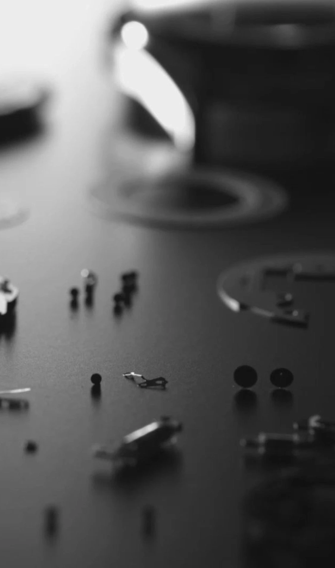 Watch parts scattered on a dark surface, monochrome, close-up shot.