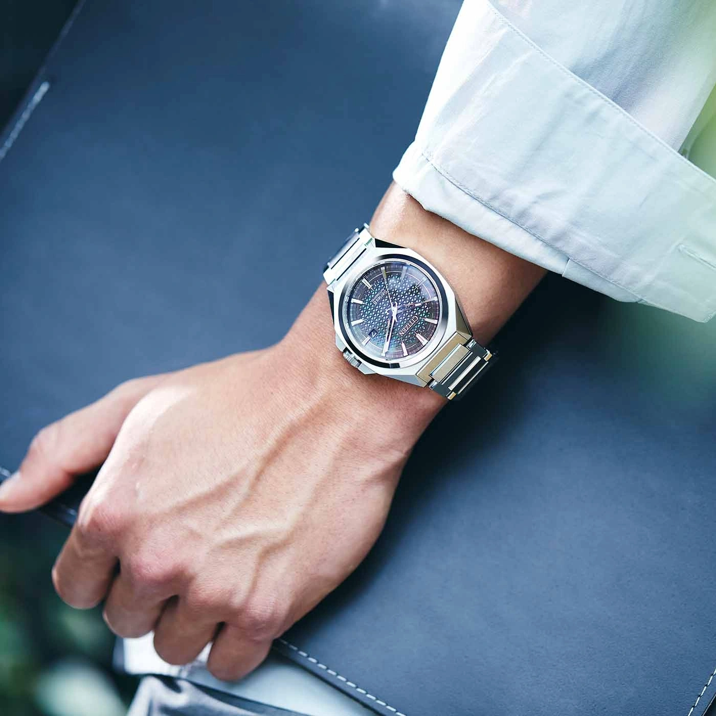 Man wearing a silver watch, holding a dark blue folder.