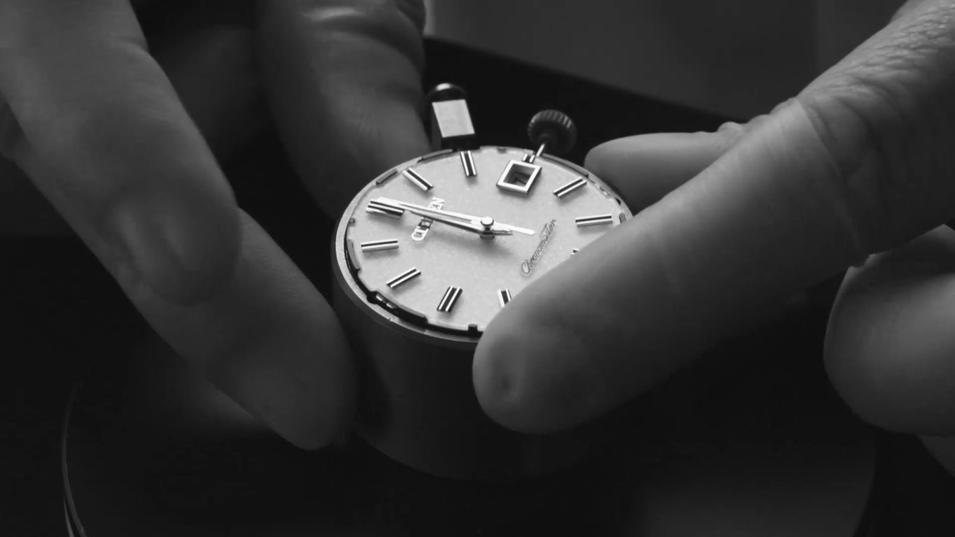 Close-up of a watch being held by two hands, watch face visible.