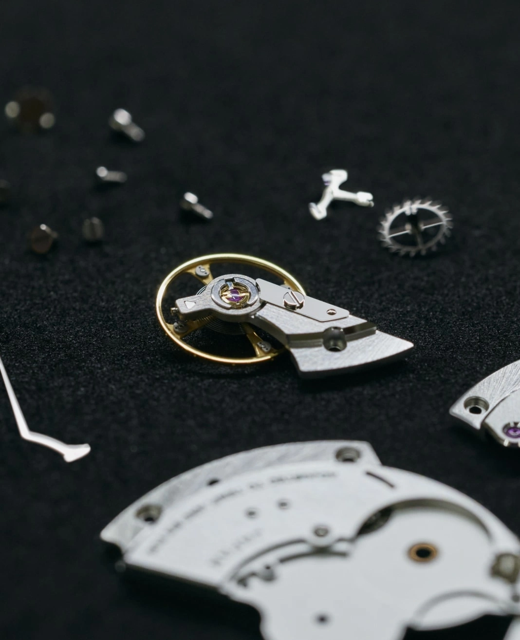Close-up of watch parts on a black surface, intricate details visible.