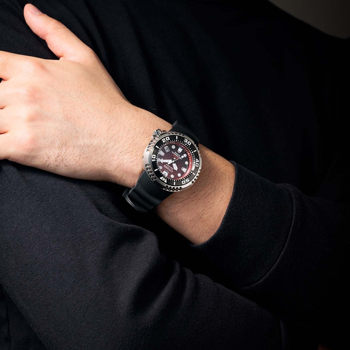 Man wearing a Citizen watch with a black strap and a red dial.