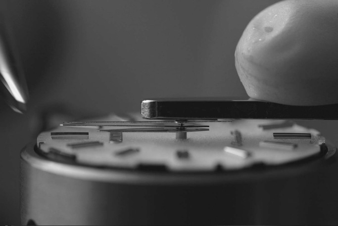 Close-up of watch mechanism being assembled with tools and precision.