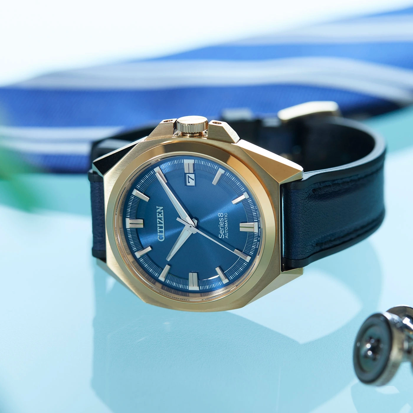 Close-up of a gold watch with a blue face and black strap.
