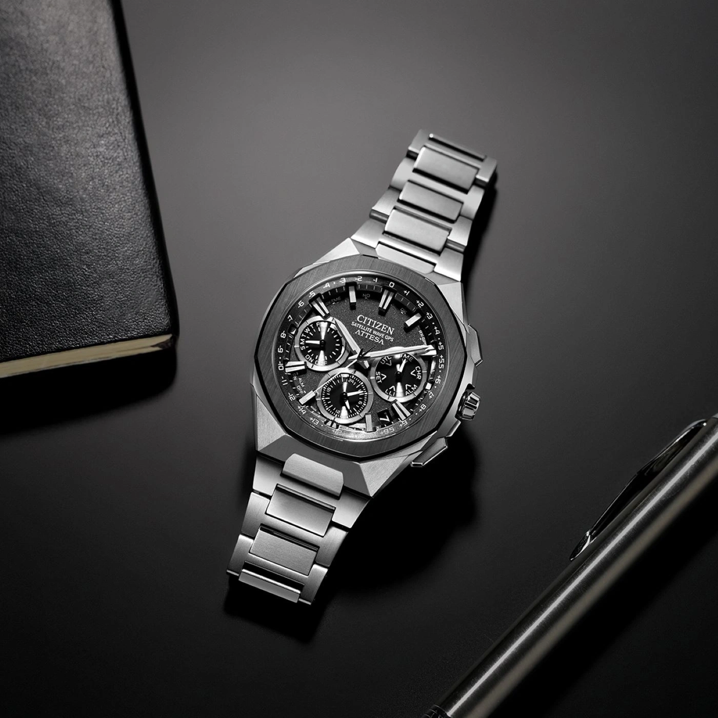 Citizen watch on a black surface with a pen and notebook.