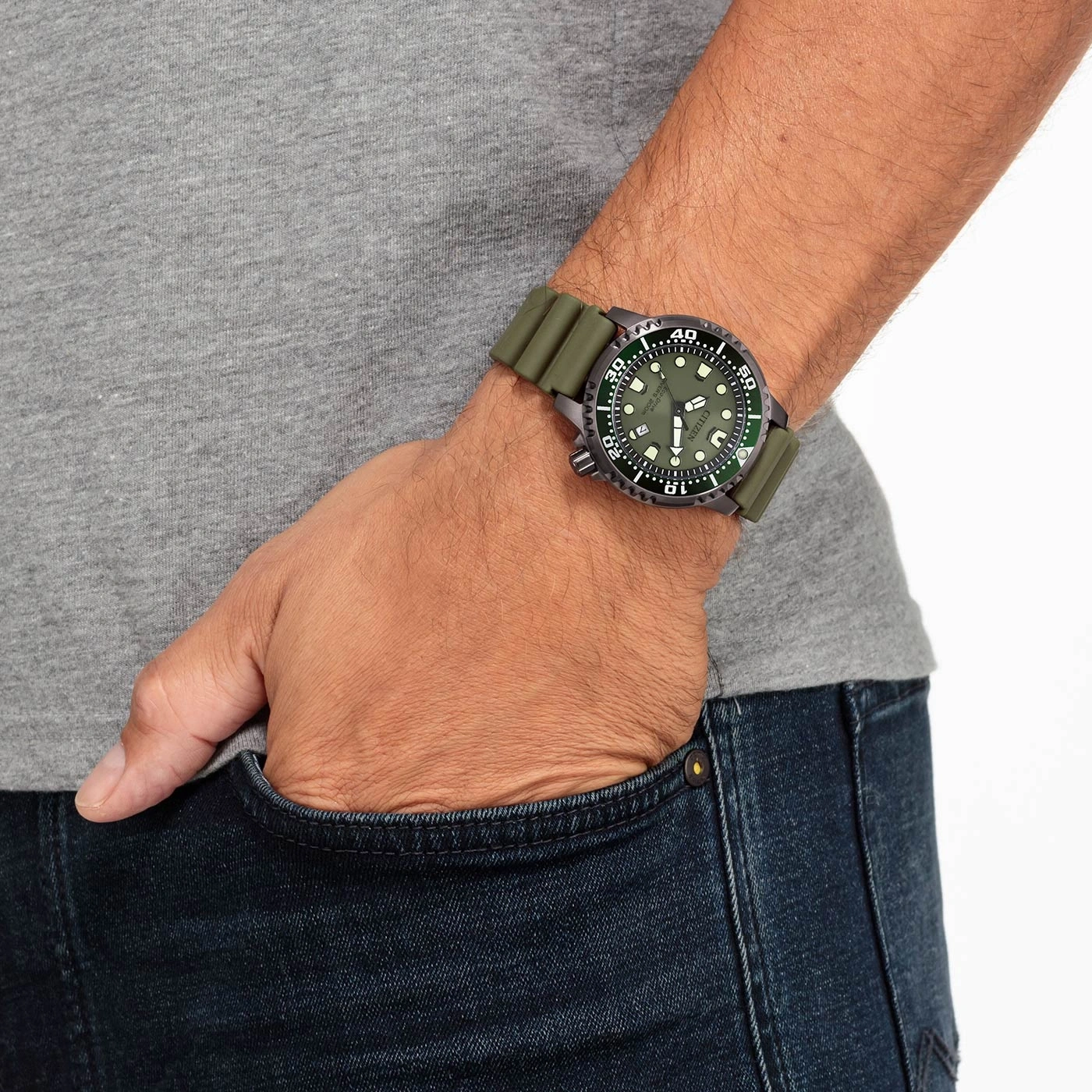Man wearing a green watch, hand in pocket, grey shirt, blue jeans.